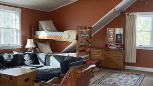 Une pièce confortable avec un lit superposé, un canapé, une chaise, une commode en bois et une petite table.