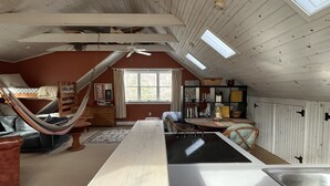 Une chambre mansardée chaleureuse, avec un lit superposé, un hamac, une table à manger et un coin cuisine.