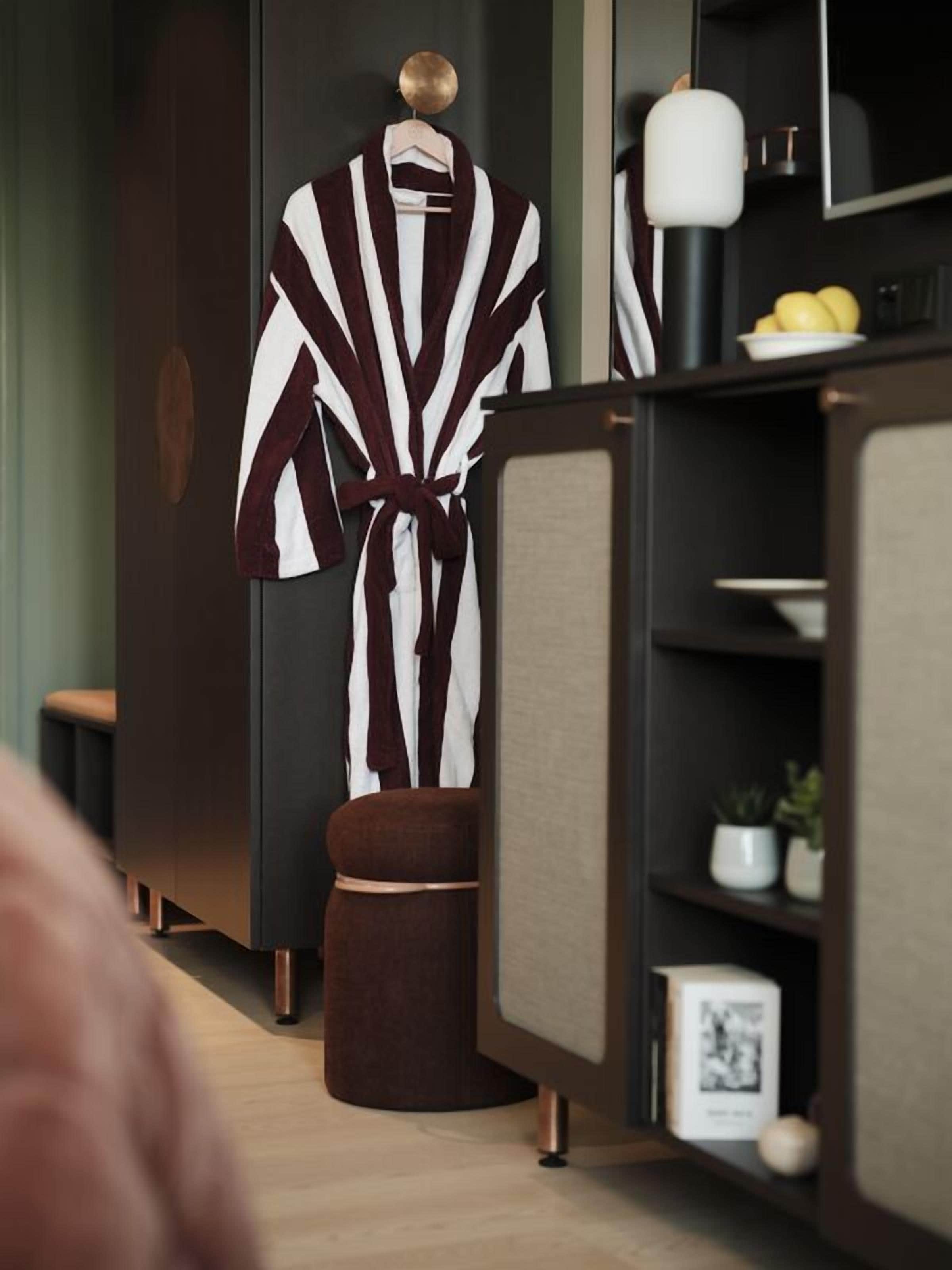 A modern bathroom with a large mirror, a robe hanging on a rack, and a small stool.