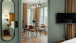 A hotel room with a bed, a TV, a dining area with chairs and a table, and a large window with curtains. - Ad Astra by Elite - Hotel, Spa & Resort (Sodertalje)
