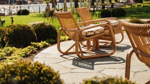 Wicker chairs and a table on a paved area with trimmed bushes and trees in the background. - Ad Astra by Elite - Hotel, Spa & Resort (Sodertalje)