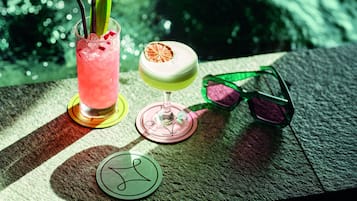 Two cocktails on a table with a pair of sunglasses and a coaster with a logo.