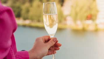 Uma pessoa segurando um copo de vinho branco, com um lago e vegetação ao fundo.