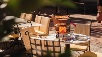 An outdoor dining area with metal chairs and tables, a tiered serving stand with food, and a glass with a drink.