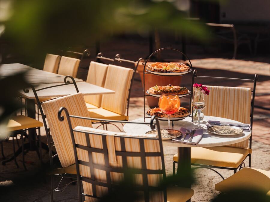 An outdoor dining area with metal chairs and tables, a tiered serving stand with food, and a glass with a drink.