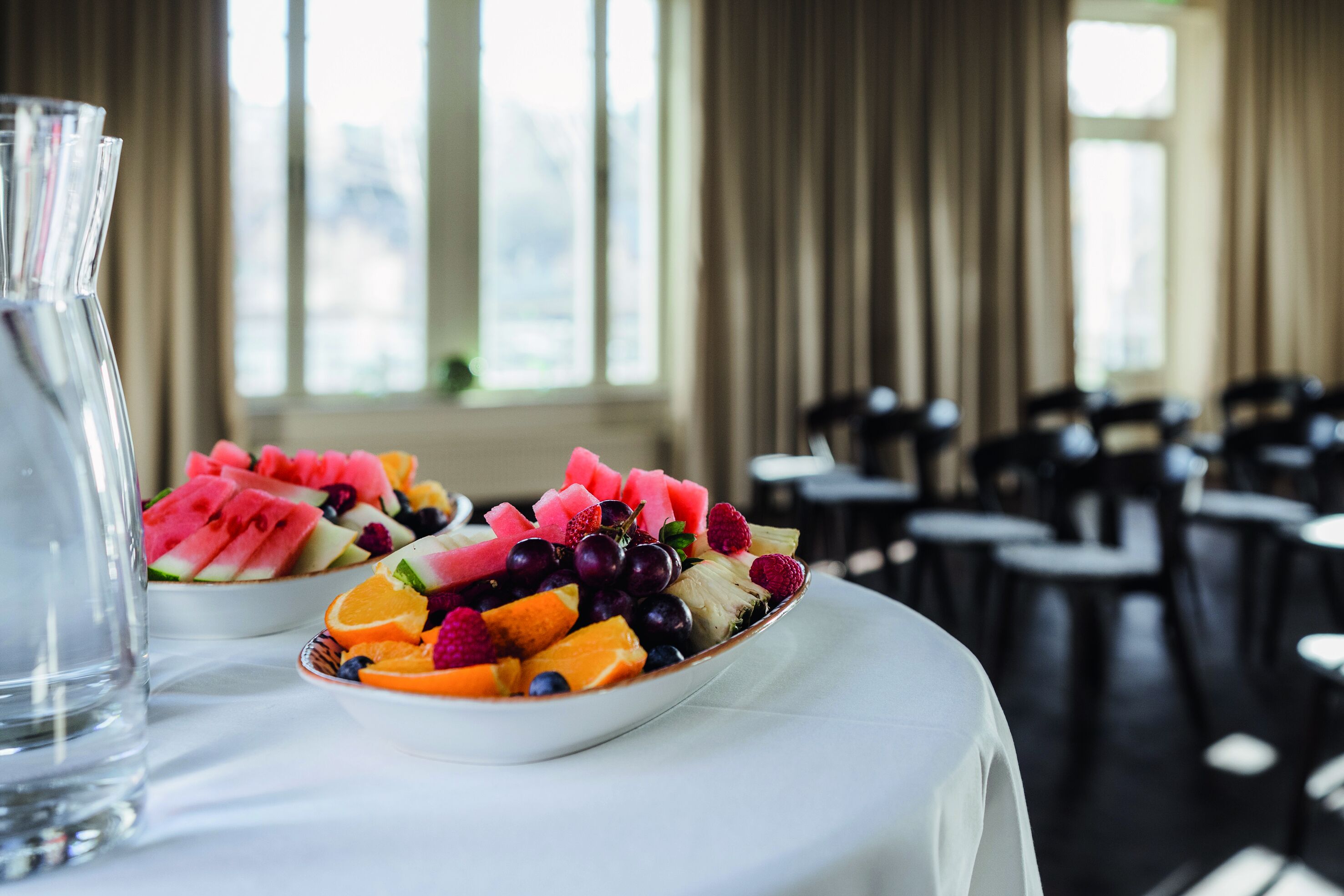 Comedor con mesas dispuestas para una comida, con una bandeja de frutas en una de ellas.