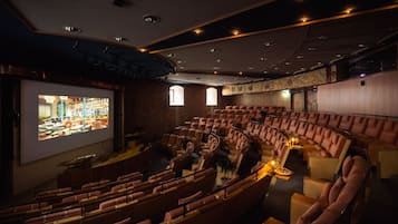 Un teatro con butacas escalonadas, una pantalla grande y una zona de bar visible a través de las ventanas.
