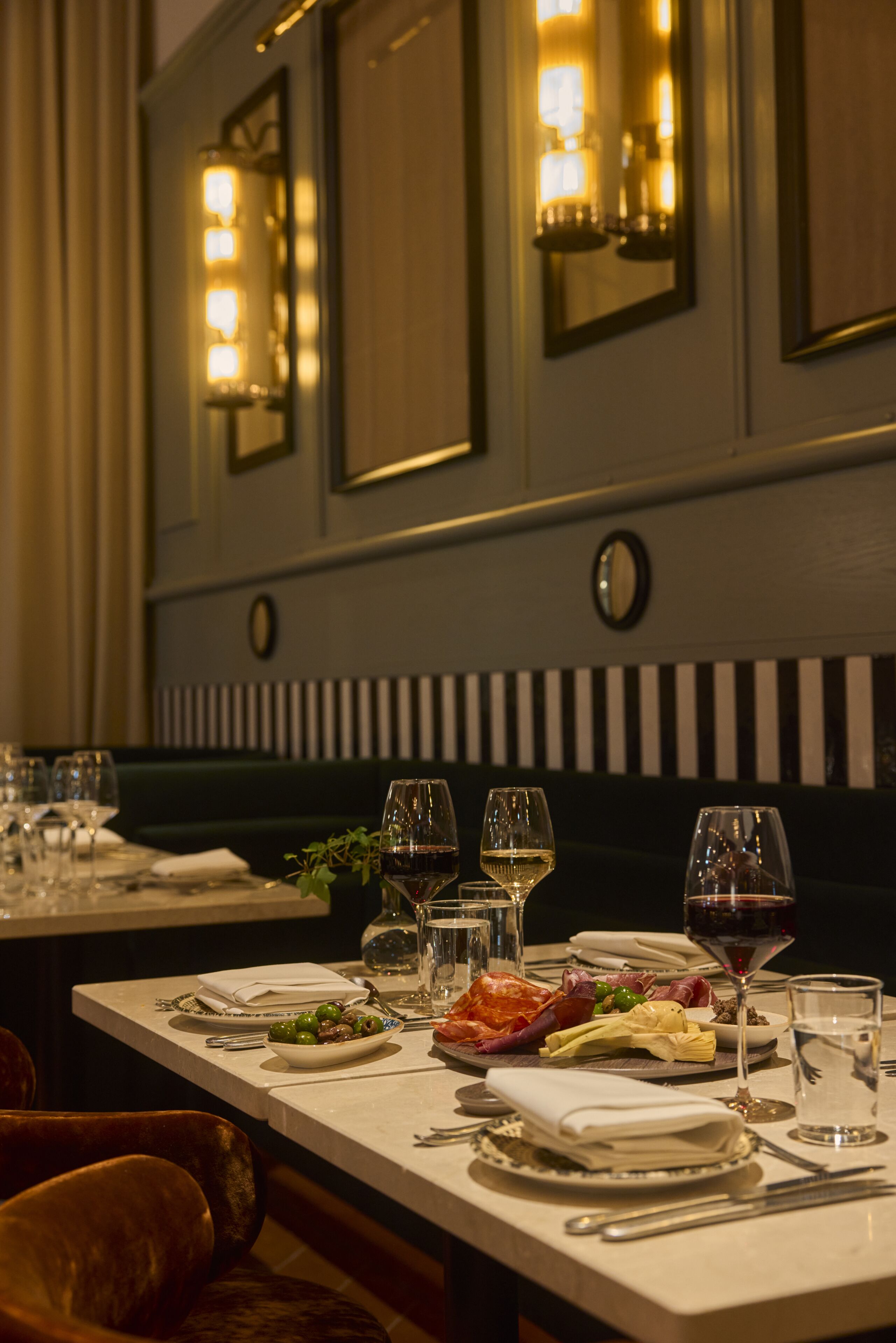 A dining table set with plates, glasses, and cutlery in a restaurant with a dark wood panel and wall-mounted lights.
