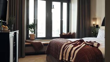 Een moderne slaapkamer met een groot raam, een bed met een gestreepte deken, een kamerplant en een bureau met een lamp.