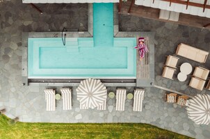 A swimming pool with a stone deck, lounge chairs, and umbrellas.