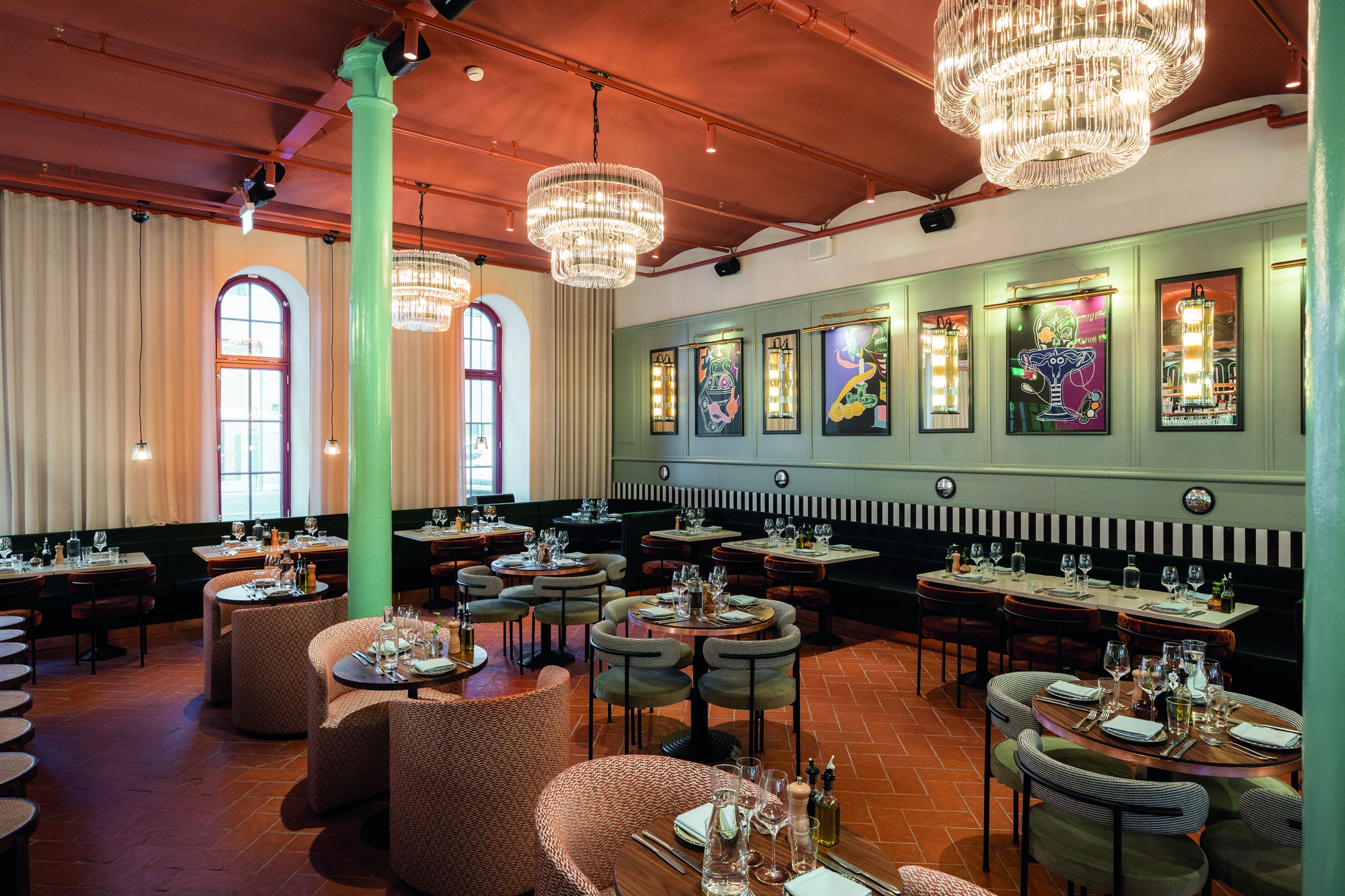 Ein Restaurant mit runden Tischen, grünen Wänden und Kristallleuchtern.
