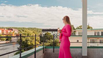Una mujer con un vestido rosa parada en un balcón con vistas a un río y edificios.