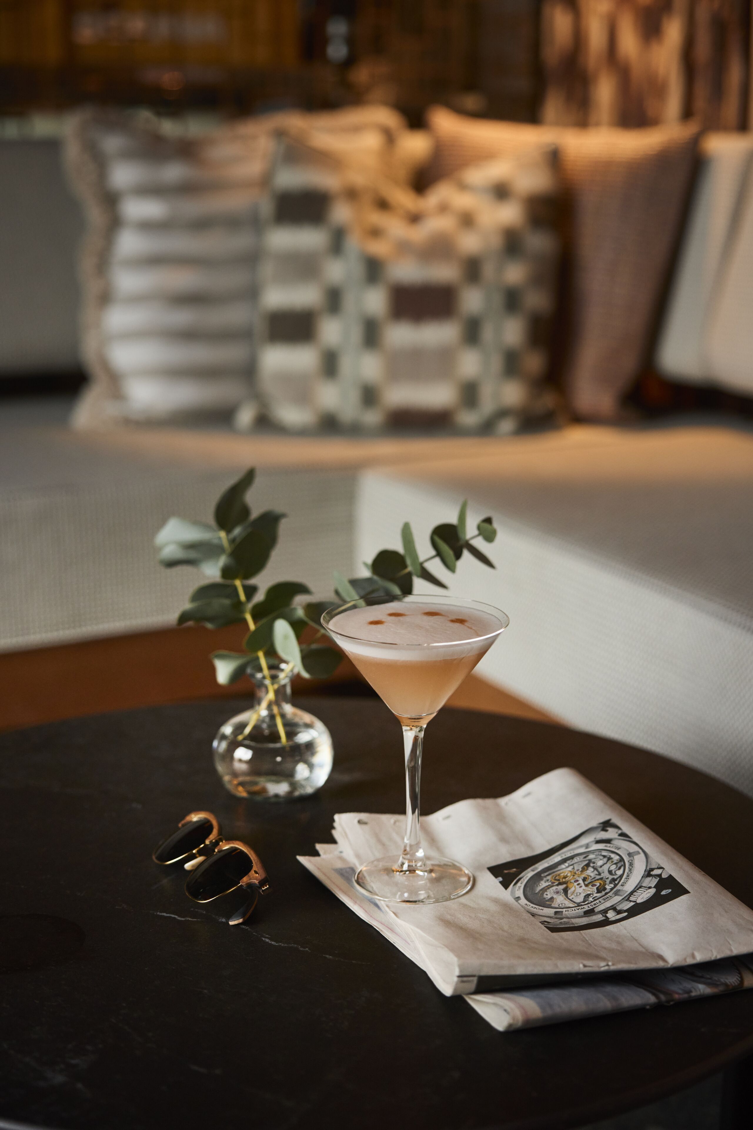 A martini glass on a table with a newspaper and a pair of sunglasses.