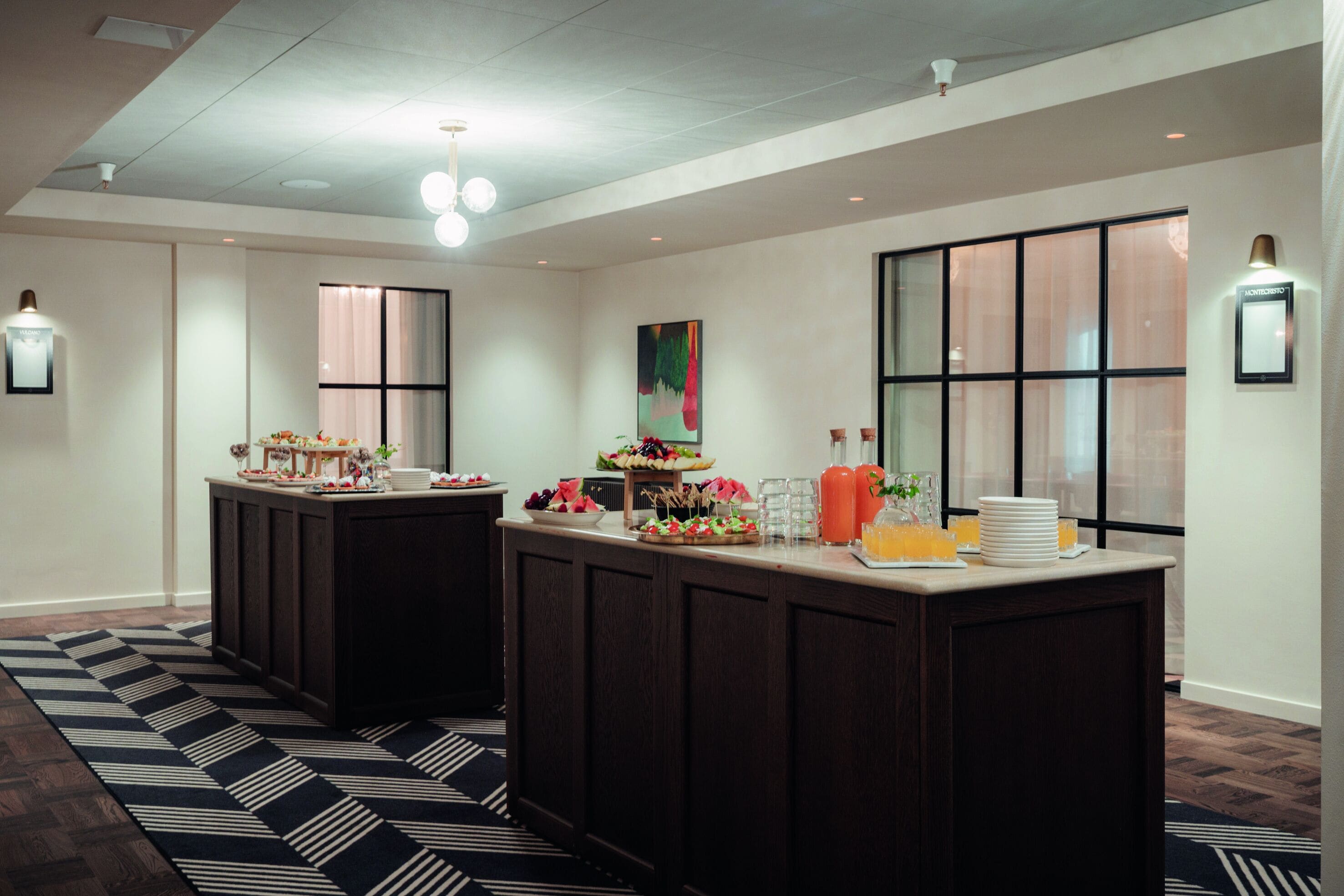 A hotel reception area with a dark wood reception desk, a patterned rug, and a large window with blinds.