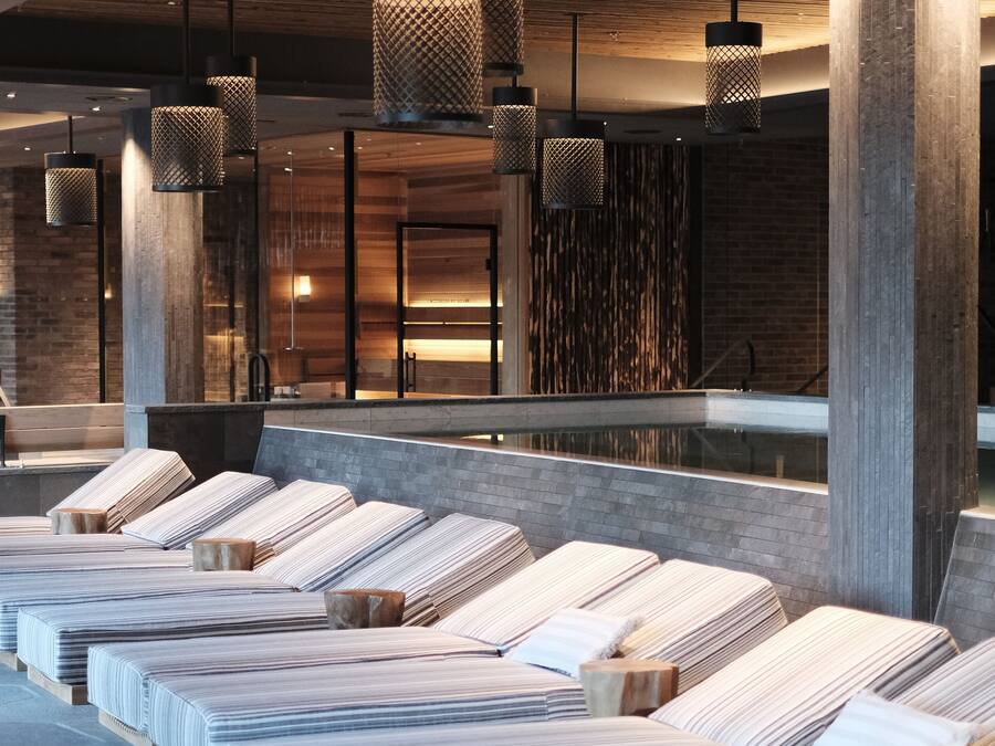 A modern spa area with multiple massage tables arranged in rows, wooden paneling on the walls, and hanging pendant lights.