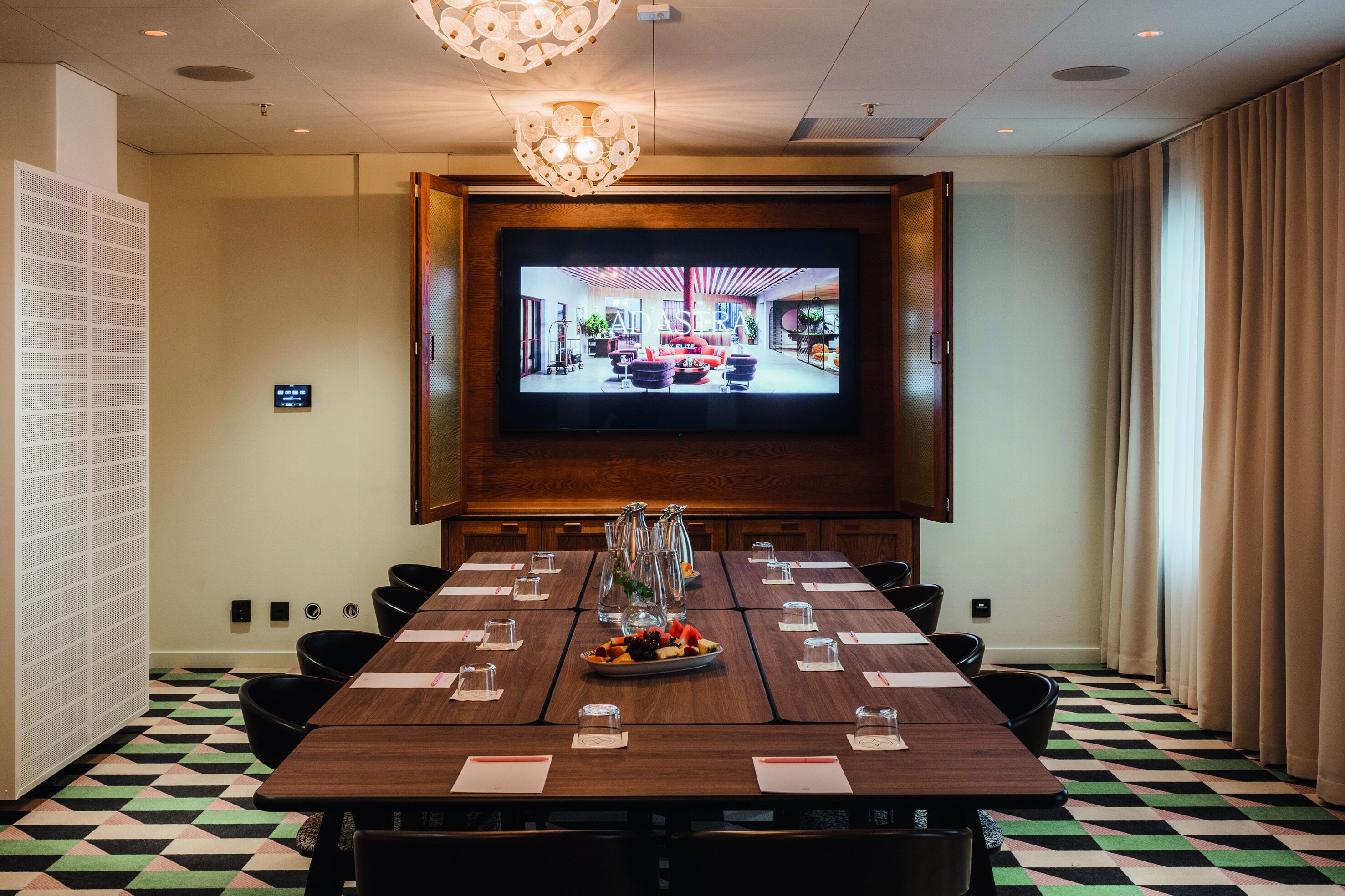 A conference room with a large screen, a wooden table, and a patterned floor.