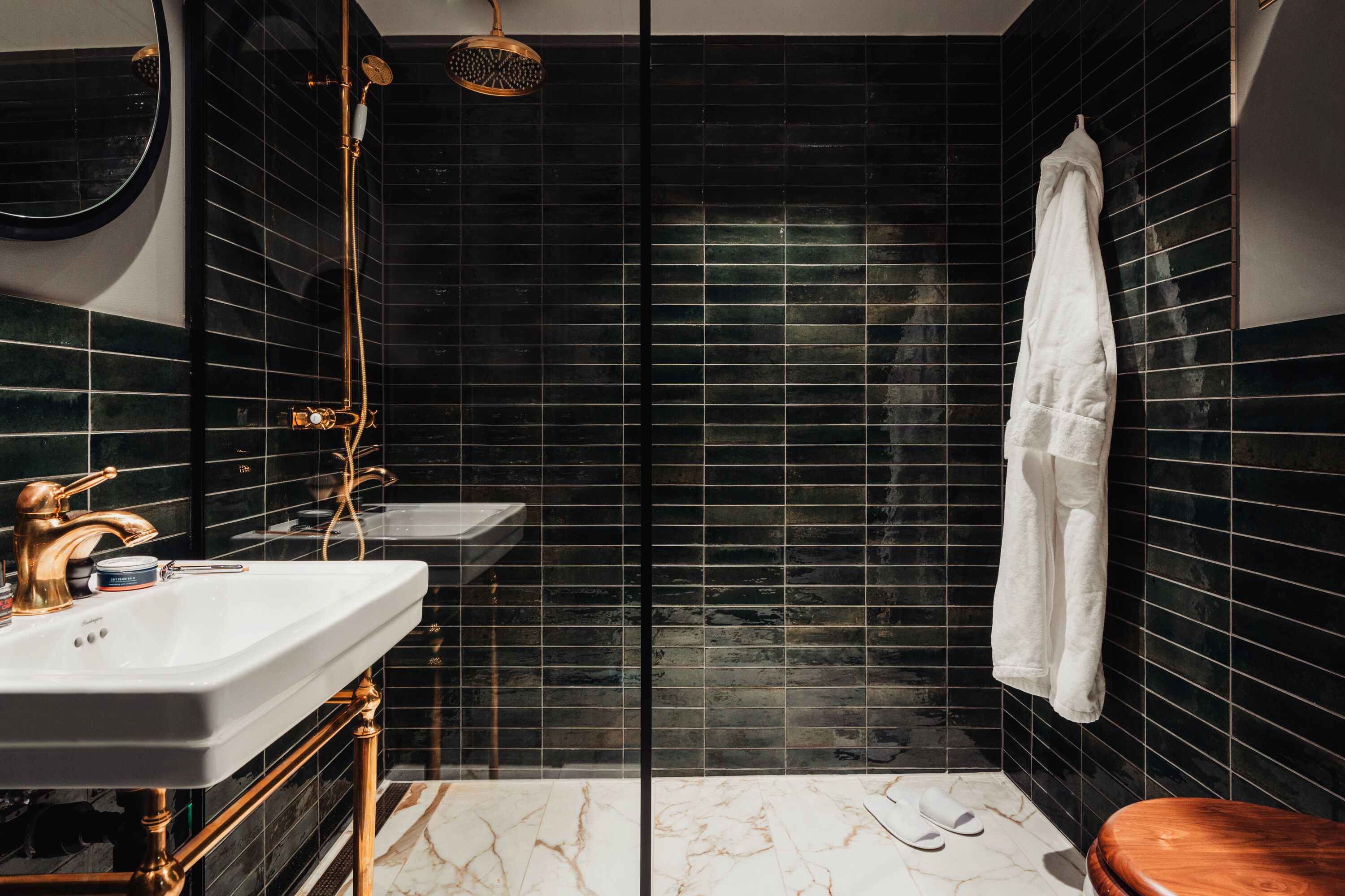 A bathroom with a white sink, gold fixtures, a wooden toilet, and a black tiled shower area.