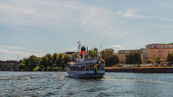 A riverboat with a flag on its mast, moving on a river with a cityscape in the background.
