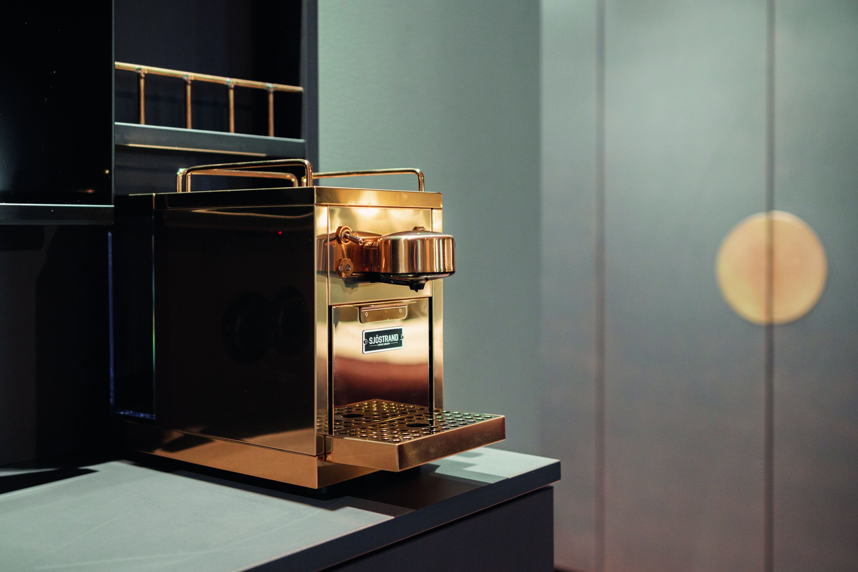 Une machine à café portant une étiquette de marque, placée sur un comptoir doté d’une base en treillis métallique.