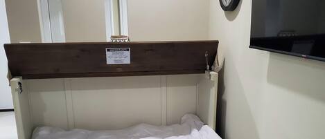A bedroom with a wooden headboard, a white bedspread, a wall clock, and two mirrors.
