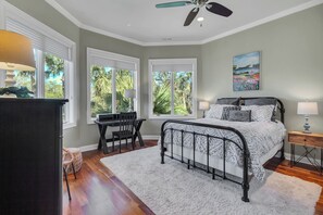A bedroom with a bed, a desk, and a chair. There are windows with views of greenery. - 8 West Beach Lagoon at The Sea Pines Resort (Hilton Head Island)