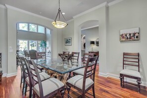 A dining area with a glass-top table surrounded by wooden chairs, a chandelier, and framed artwork on the walls. - 8 West Beach Lagoon at The Sea Pines Resort (Hilton Head Island)