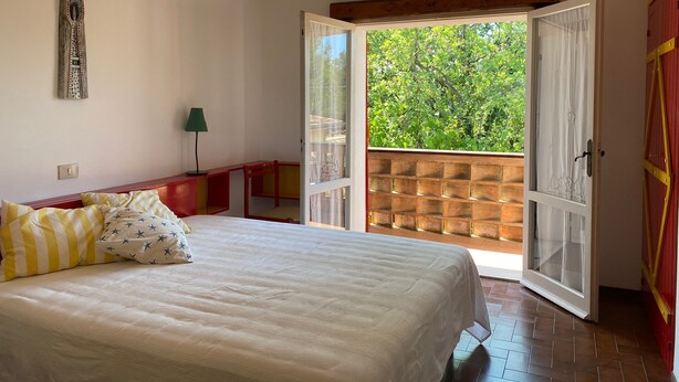 A bedroom with a bed, a nightstand, a lamp, and an open door leading to a balcony with a view of greenery. - La Casa di Paola - Four Bedroom Apartment, Sleeps 8 (Panoramica)