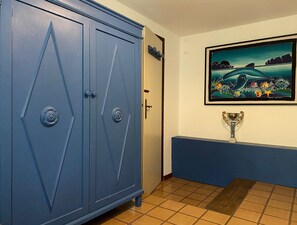 A room with a blue wardrobe, a door, a framed painting of a landscape, and a trophy on a stand.