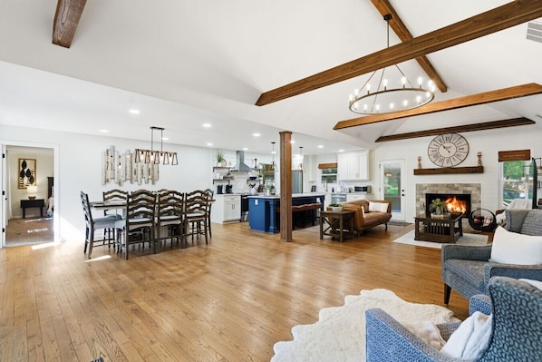 Un vaste espace de vie doté d’un plancher en bois, un coin repas avec une table et des chaises en bois, une cuisine avec des meubles blancs et une cheminée.