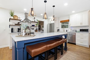 Une cuisine moderne dotée d’un grand îlot central, de luminaires suspendus, d’appareils électroménagers en acier inoxydable et d’un mur d’accent bleu.