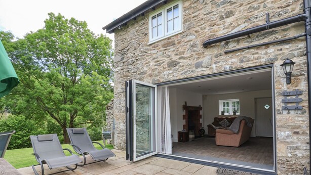 A stone building with a glass door leading to a living area with a fireplace, a sofa, and a table.