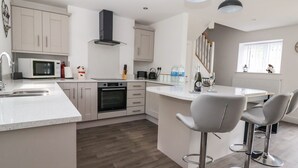 A modern kitchen with a central island, bar stools, a microwave, oven, and a staircase leading to another level.