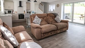 A modern living room with a brown sofa, patterned cushions, and a white ottoman.