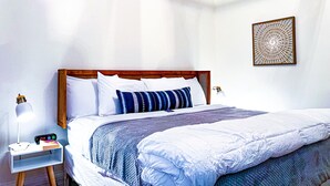 A neatly made bed with white and blue bedding, a bedside table with a lamp and a digital clock, and a decorative wall piece. - Set within a beautifully restored 19th century home in the heart of Watkins Glen (Watkins Glen)