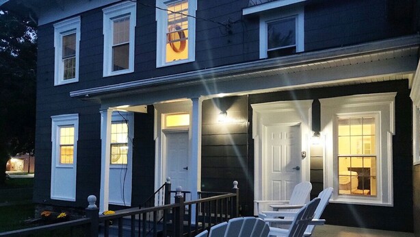 A two-story house with a porch, white doors, and a small outdoor seating area with Adirondack chairs. - Set within a beautifully restored 19th century home in the heart of Watkins Glen (Watkins Glen)