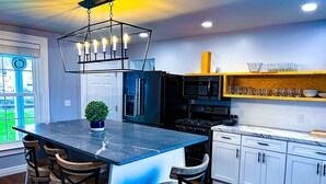 A modern kitchen with a central island, bar stools, a built-in oven, and a microwave. - Set within a beautifully restored 19th century home in the heart of Watkins Glen (Watkins Glen)