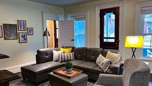 A living room with a sectional sofa, a patterned armchair, a coffee table with a plant, and a lamp. - Set within a beautifully restored 19th century home in the heart of Watkins Glen (Watkins Glen)