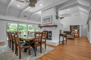 A spacious dining area with a high ceiling and large windows, a fireplace, and a cozy seating area with a sofa and side table.