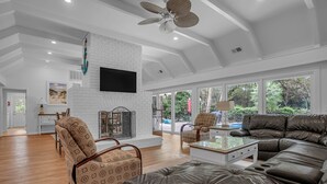 A spacious living room with a white brick fireplace, leather sofas, and large windows offering a view of the outdoors. - 8 Wood Ibis at The Sea Pines Resort (Hilton Head Island)