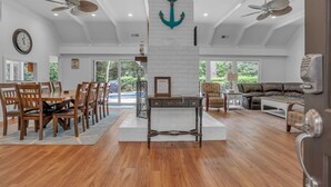 A spacious living area with a dining table, chairs, and a sofa. There are ceiling fans, a fireplace, and large windows. - 8 Wood Ibis at The Sea Pines Resort (Hilton Head Island)