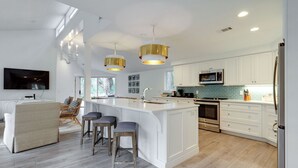 A modern kitchen with white cabinetry, a large island with bar stools, stainless steel appliances, and pendant lighting. - 9 Baynard Cove Road at The Sea Pines Resort (Hilton Head Island)