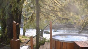 A wooden deck with a hot tub surrounded by trees and a river.