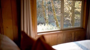 A bedroom with a window overlooking a forest.
