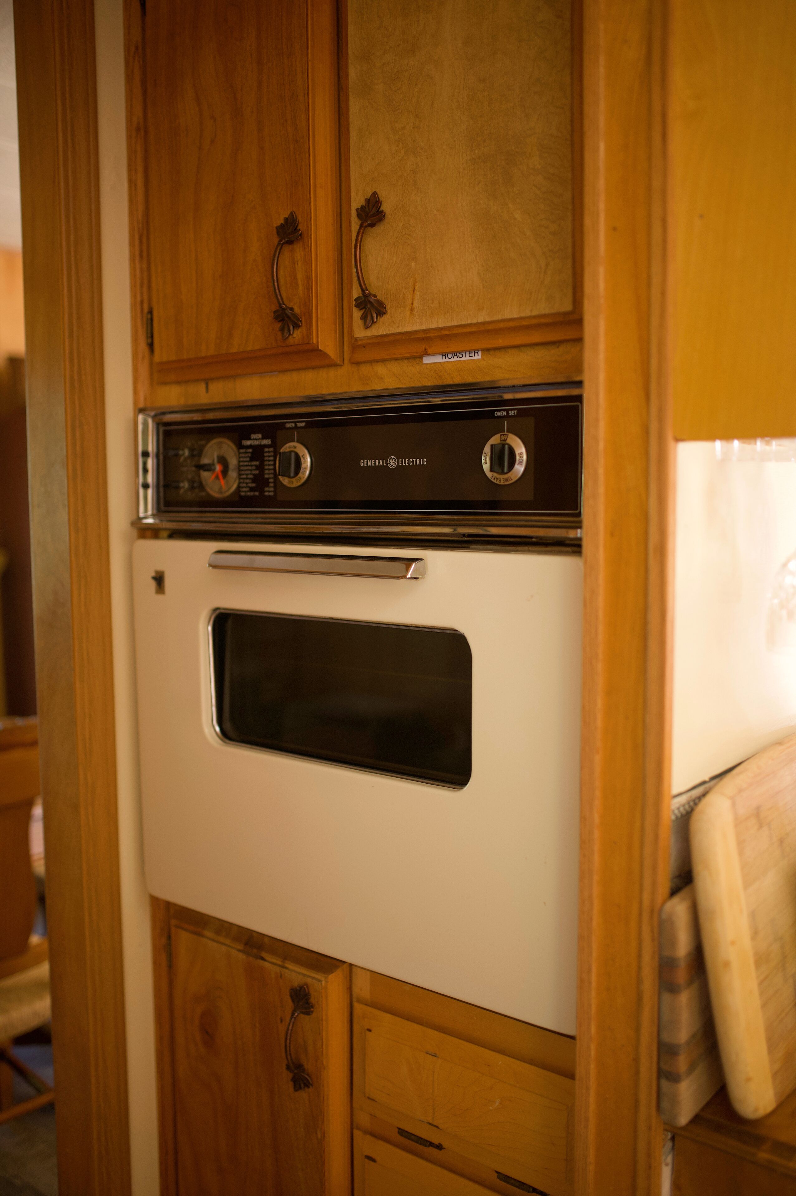 A white General Electric oven with a control panel, located in a wooden cabinet with a handle.