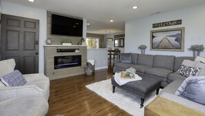 Ein modernes Wohnzimmer mit Kamin, grauen Sofas und einem 'Welcome'-Schild.