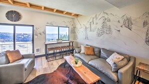 Uma sala de estar moderna com uma janela grande, um sofá, uma mesa de centro e um mural de montanhas.