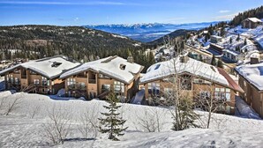 Estância de montanha coberta de neve com edifícios modernos, incluindo uma hospedaria de dois andares com um teleférico visível ao fundo.