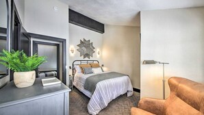 Quarto de hotel com cama, escrivaninha com planta, luminária e cadeira.
