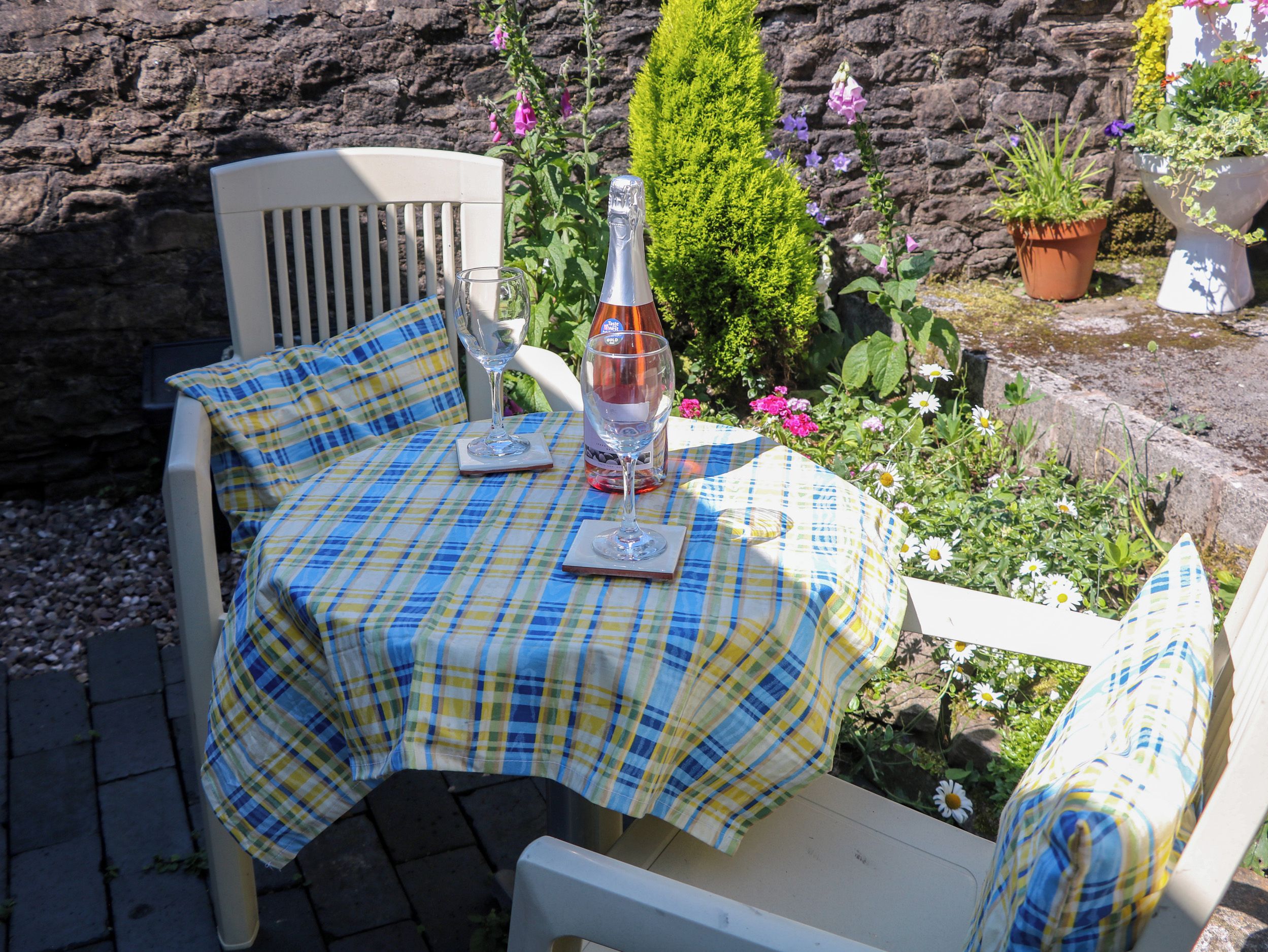 A table set outdoors with a checkered tablecloth, a bottle, and glasses.
