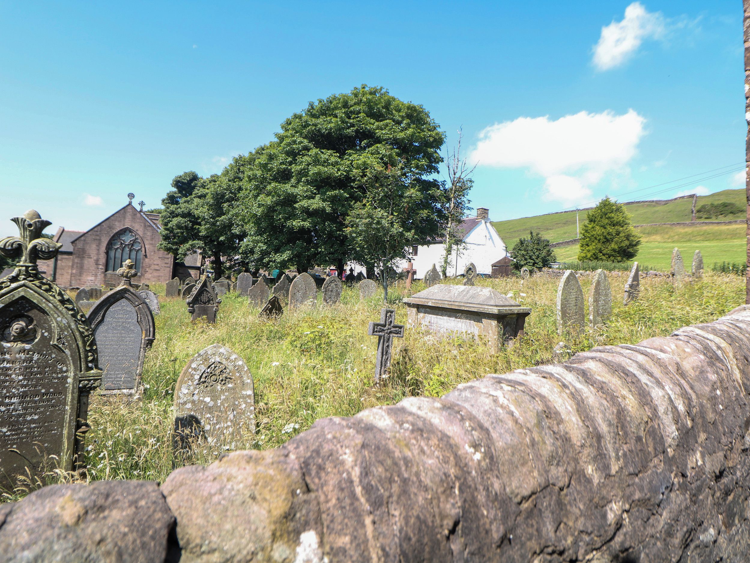 A cemetery with gravestones, a church, and a large tree.